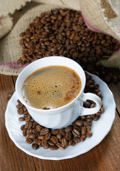 Cup with coffee on the table next to coffee beans — Stock Photo, Image