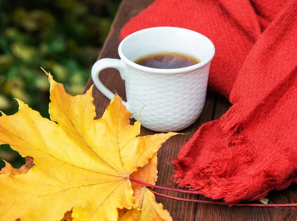 Tazza di tè sul tavolo con sciarpa e foglie gialle — Foto Stock