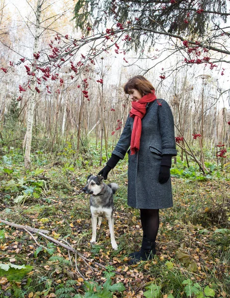 woman standing among the trees and petting the dog