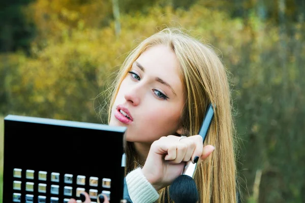 Girl puts makeup on the street against the background of autumn — Stock Photo, Image