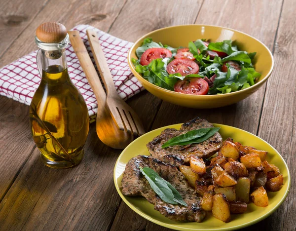 Gebakken aardappelen met vlees en een plaat van salade op tafel — Stockfoto