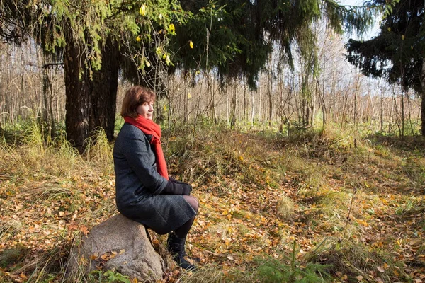 Middle-aged woman sitting on a rock in an autumn forest — Stock Photo, Image