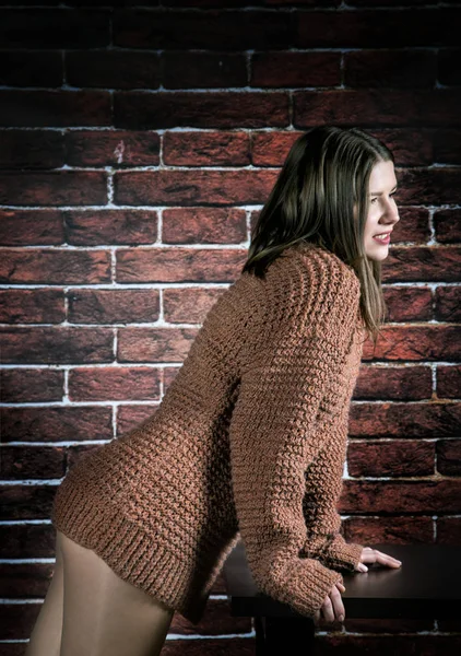 Дівчина в светрі спирається на журнальний столик на цегляному фоні стіни — стокове фото