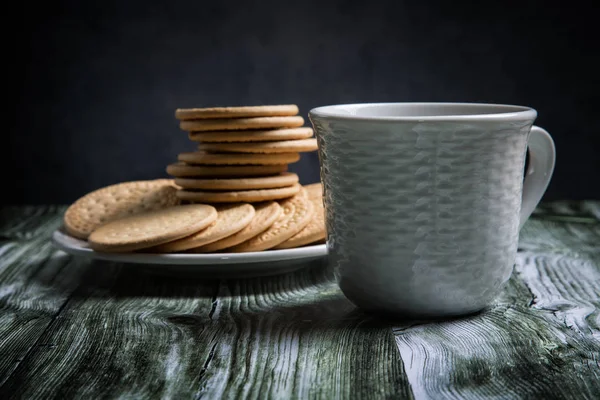 一杯茶和一叠饼干放在旧桌子上 — 图库照片