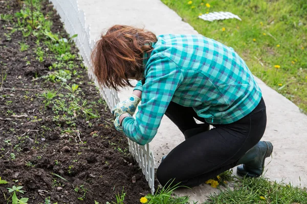 Woman fixing a decorative fence on a flower bed — Stock Photo, Image
