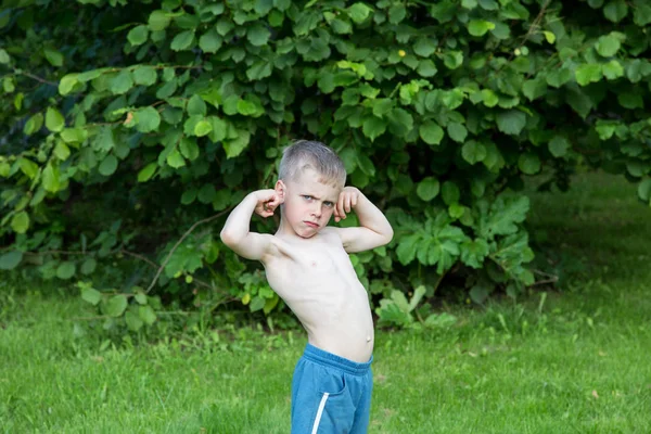 Mały chłopiec pokazuje biceps w ogrodzie w letni dzień — Zdjęcie stockowe