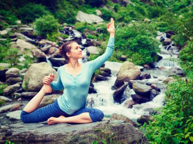 Tropikal şelalede yoga yapan formda bir kadın.