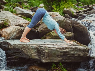 Genç, formda bir kadın tropik şelalede yoga yapıyor.