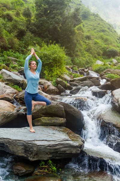 Женщина в йоге Асана Vrikshasana дерево позировать у водопада на открытом воздухе — стоковое фото