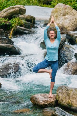 Yogadaki kadın, Vrikshasana ağacı, şelalede poz veriyor.