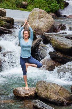 Yogadaki kadın, Vrikshasana ağacı, şelalede poz veriyor.