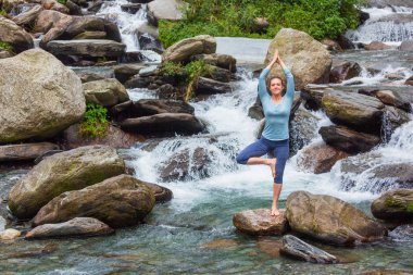 Yogadaki kadın, Vrikshasana ağacı, şelalede poz veriyor.