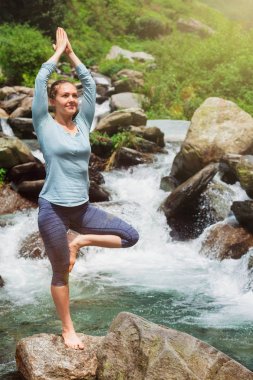 Yogadaki kadın, Vrikshasana ağacı, şelalede poz veriyor.
