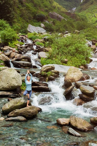 Kvinna i yoga asana Vrikshasana träd poserar vid vattenfall utomhus — Stockfoto