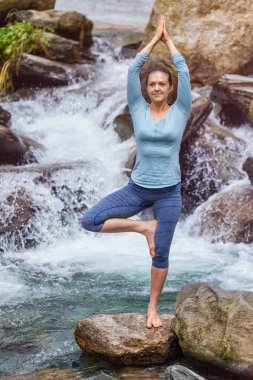 Yogadaki kadın, Vrikshasana ağacı, şelalede poz veriyor.