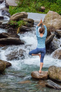 Yogadaki kadın, Vrikshasana ağacı, şelalede poz veriyor.