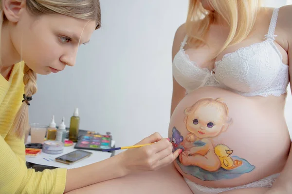 Joven artista de maquillaje dibujar a un niño en el vientre —  Fotos de Stock