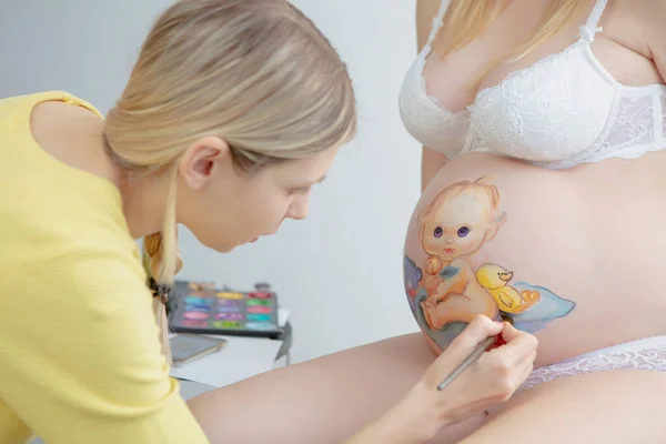 Nice makeup artist draws a baby on the belly — Stock Photo, Image
