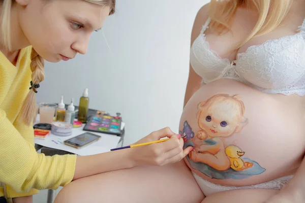 Maquilleuse dessine un bébé mignon sur le ventre — Photo