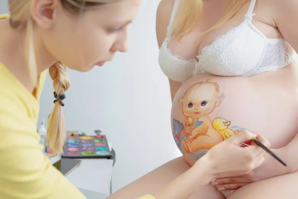 Young makeup artist draws a baby on the belly — Stock Photo, Image