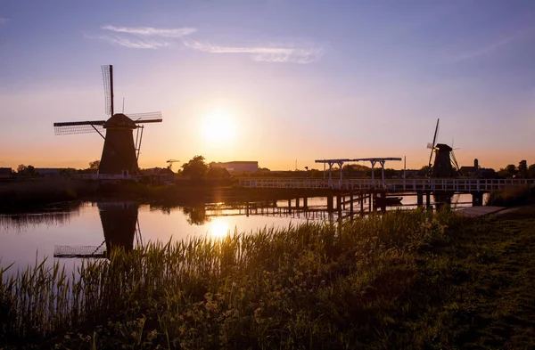 Puesta de sol con molinos de viento holandeses tradicionales y un puente de madera en K —  Fotos de Stock