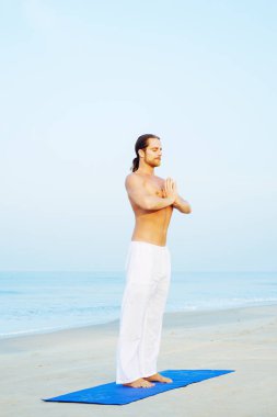 Mat 'in atletik adamı plajda yoga yapıyor.