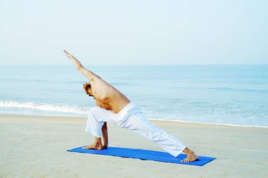 Mat 'in atletik adamı plajda yoga yapıyor.