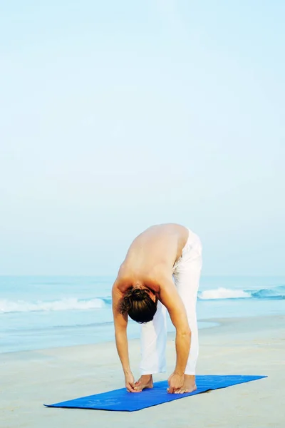 Athletic Man på Mat gör Yoga på stranden Stockfoto