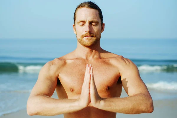 Athletic Man på Mat gör Yoga på stranden Stockfoto