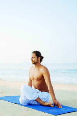 Mat 'in atletik adamı plajda yoga yapıyor.