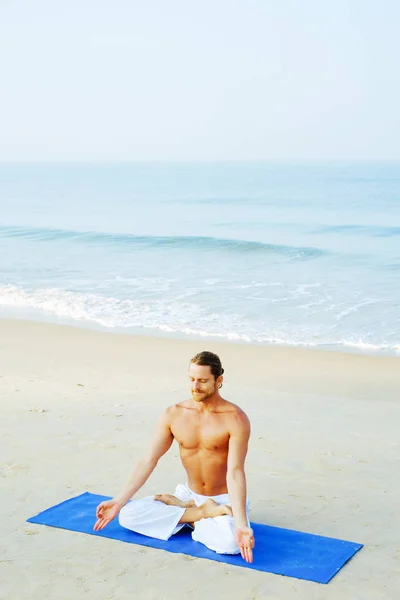 Athletic Man på Mat gör Yoga på stranden Royaltyfria Stockbilder