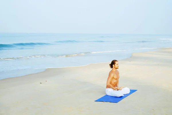 Athletic Man på Mat gör Yoga på stranden Royaltyfria Stockbilder