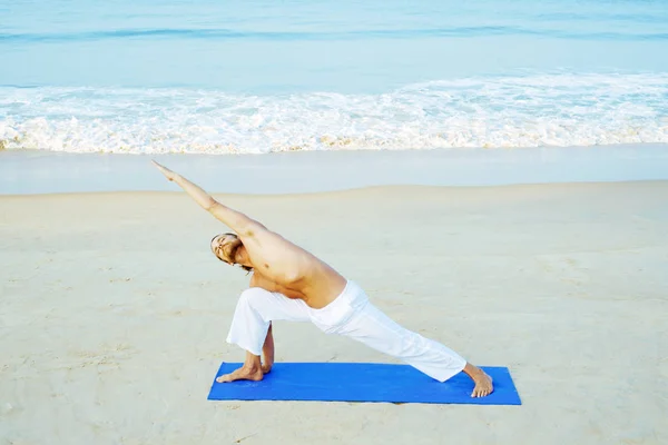 Athletic Man på Mat gör Yoga på stranden Stockbild