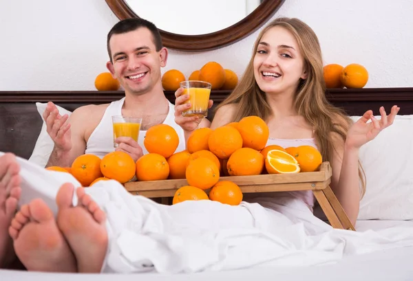 Erkek ve kız arkadaş yatakta sıkılmış portakal suyu içiyor. — Stok fotoğraf