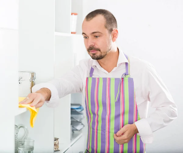 Young man in apron cleaning shelves — Stock Photo, Image
