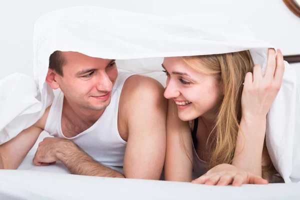 Jovem casal na cama coberto com shee — Fotografia de Stock