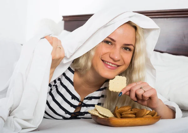 Porträt einer Frau, die Kekse unter Bettdecke isst — Stockfoto