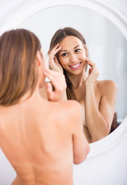 Mulher nua atentamente olhando para si mesma no espelho — Fotografia de Stock