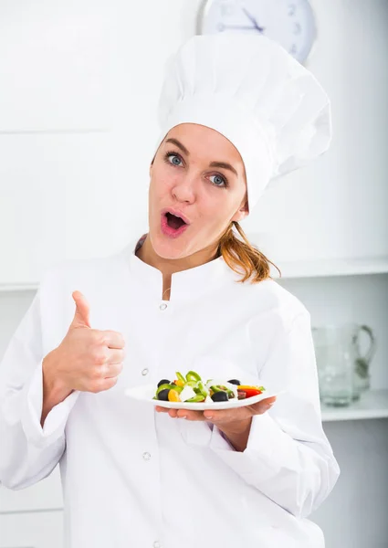 Lány szakács kalap és fehér kabát mutatja saláta — Stock Fotó