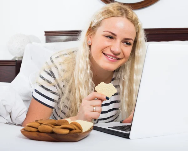 Молодая женщина с ноутбуком и печеньем в постели — стоковое фото