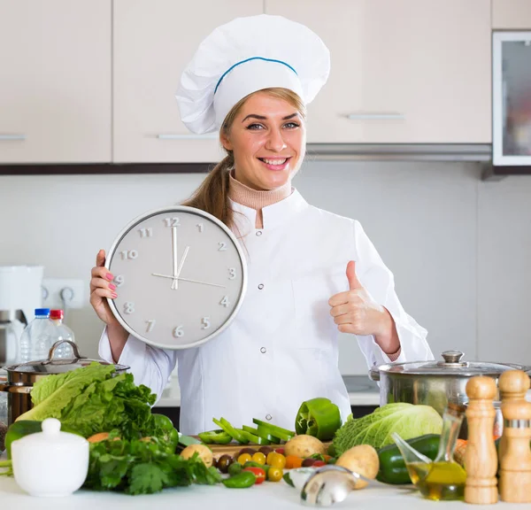 Vrolijke vrouwelijke kok met klok en groenten in de keuken — Stockfoto