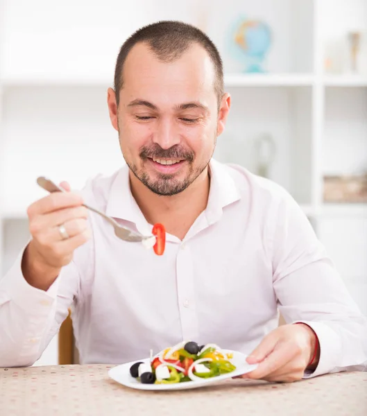 Positive young man eating greek salad — Stock Photo, Image