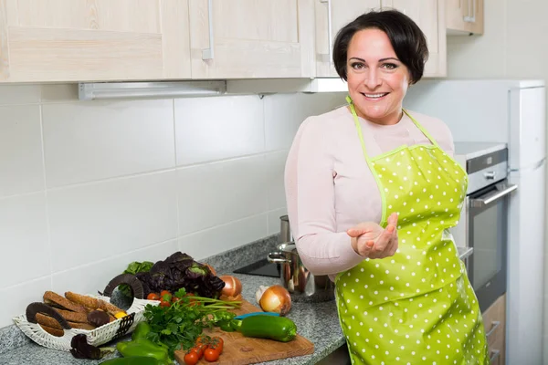 Mujer de mediana edad en delantal posando cerca de la tapa de la cocina —  Fotos de Stock