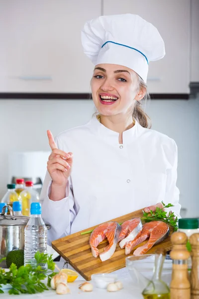 Gelukkig vrouwelijke kok poseren met zalm filets in keuken — Stockfoto