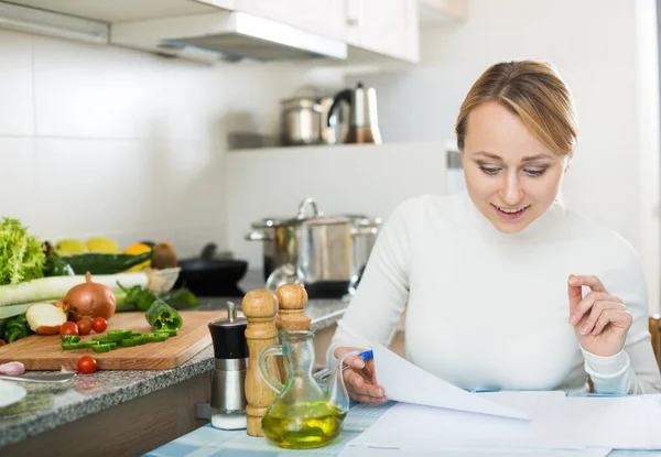 Vrolijke huisvrouw ondertekening van documenten in keuken — Stockfoto