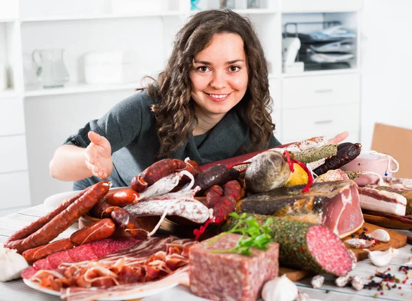 La donna costa vicino a tavolo su cui salsicce e carne affumicata — Foto Stock