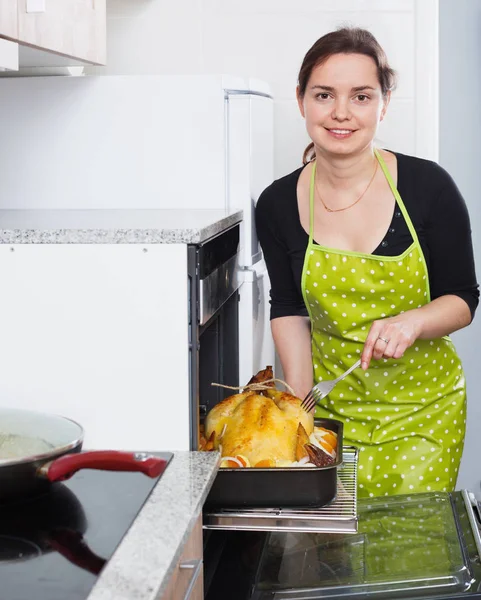 Smiling woman roasting cockerel for dinner — ストック写真