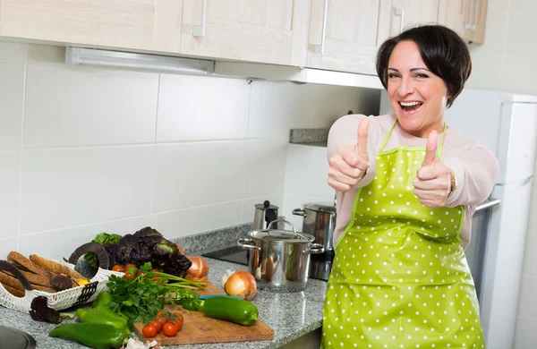 Mujer de mediana edad en delantal posando cerca de la tapa de la cocina — Foto de Stock
