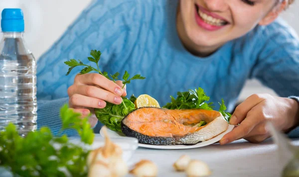 Cheerful young woman with fried rainbow trout indoors — Stock Photo, Image