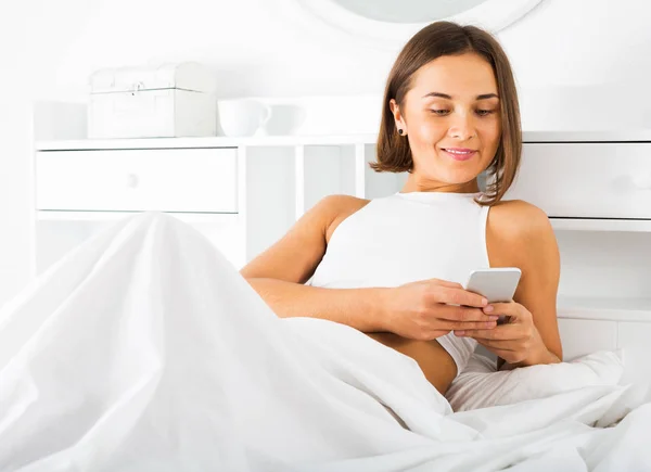 Kobieta korzystająca z telefonu w łóżku — Zdjęcie stockowe
